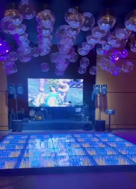 Painel de LED exibindo homenagem de 15 anos, com esferas iluminadas no teto e pista de LED azul à frente