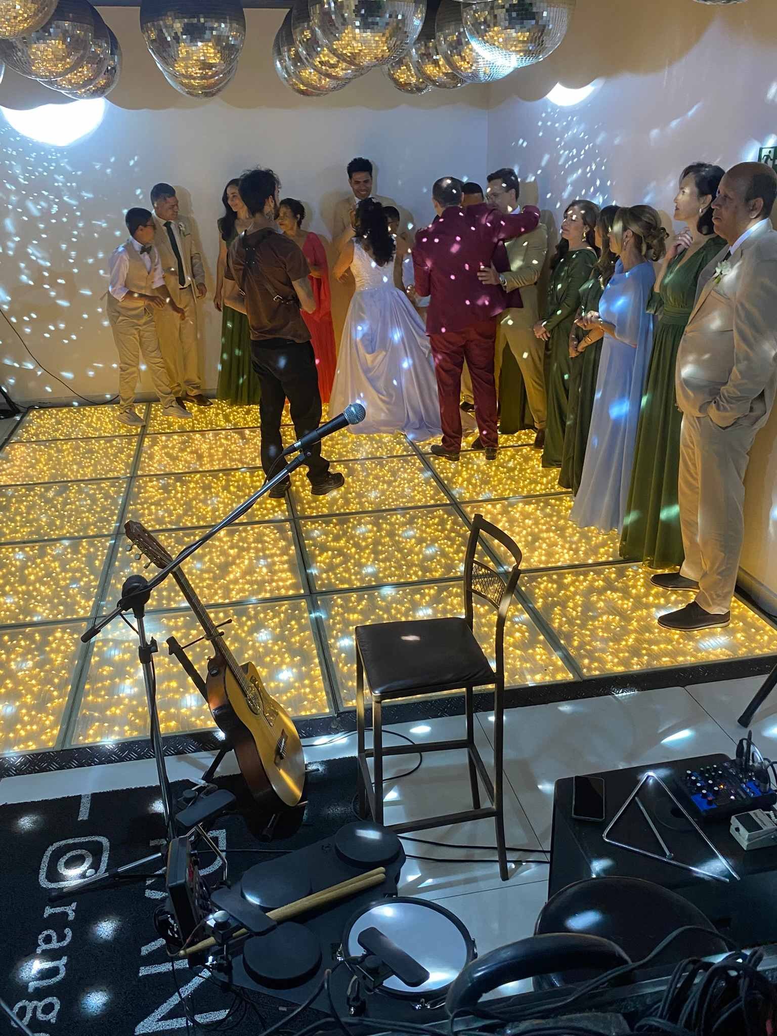 Noivos e padrinhos na pista de LED dourada de um casamento, com globos espelhados no teto e reflexos de luz pelas paredes