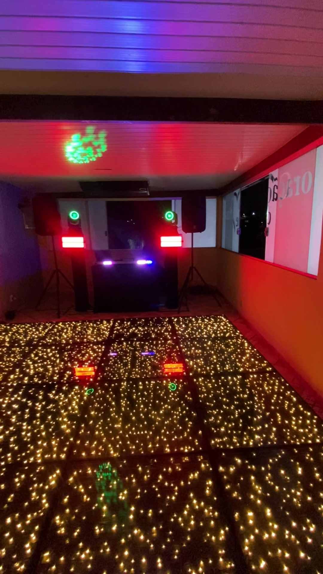 Pista de LED dourada diante da cabine de DJ, com caixas de som, moving heads e strobos iluminando o salão
