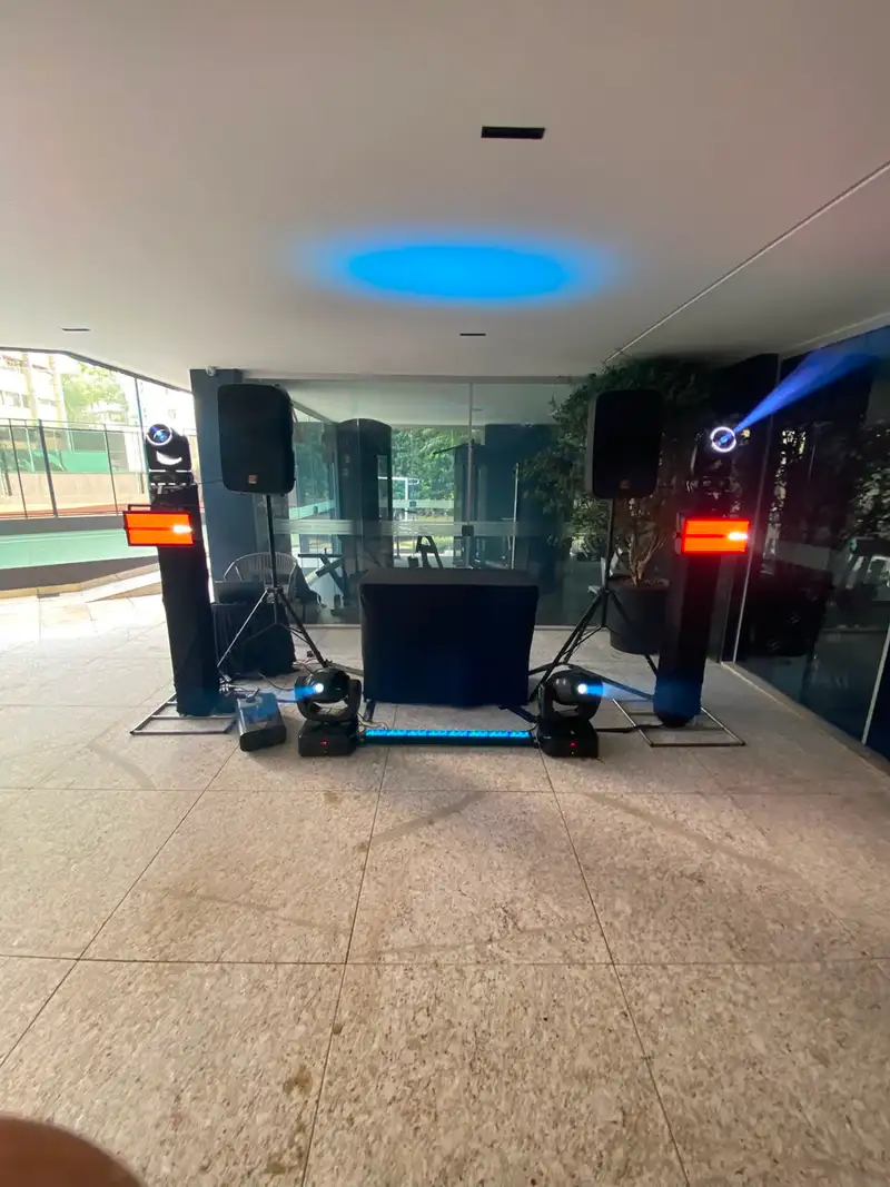 Caixas de som em tripé, moving heads, strobos e cabine de DJ montados em área coberta de condomínio