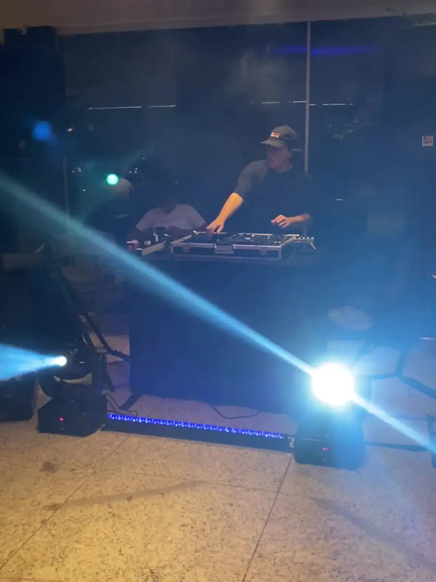 A mesma cabine à noite, com o DJ tocando, feixes dos moving heads e a barra de LED acesa