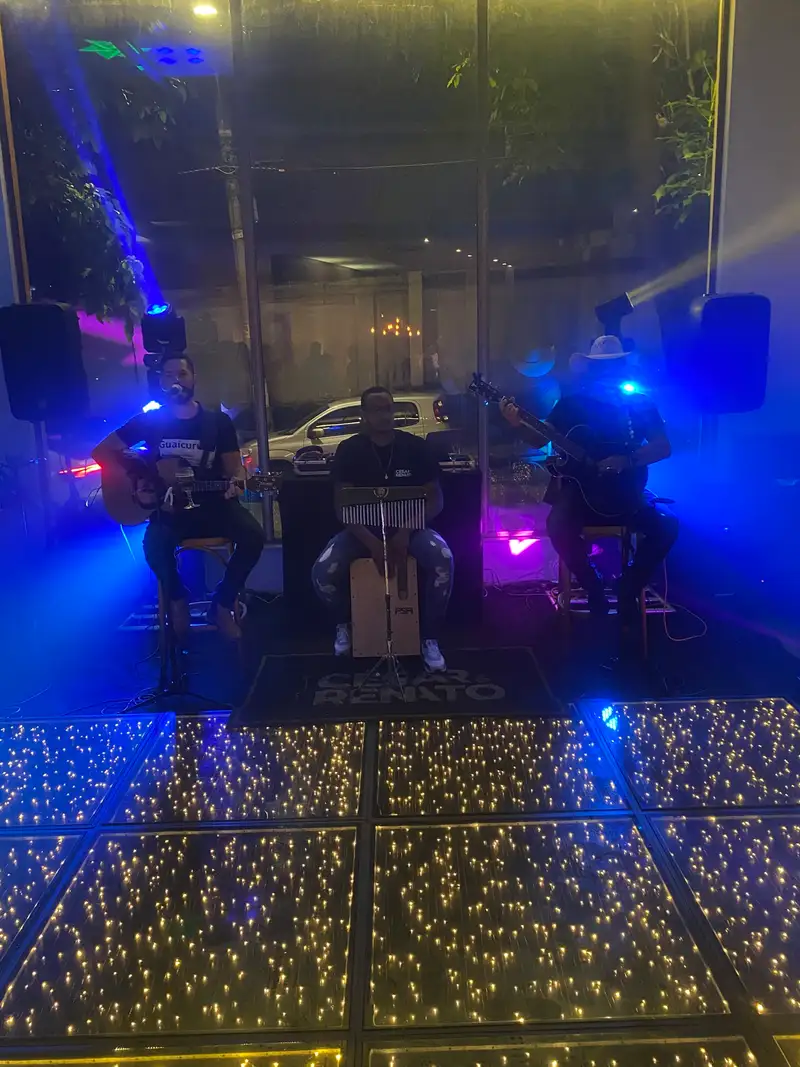 Trio acústico tocando atrás de uma pista de LED, com luz azul e violeta