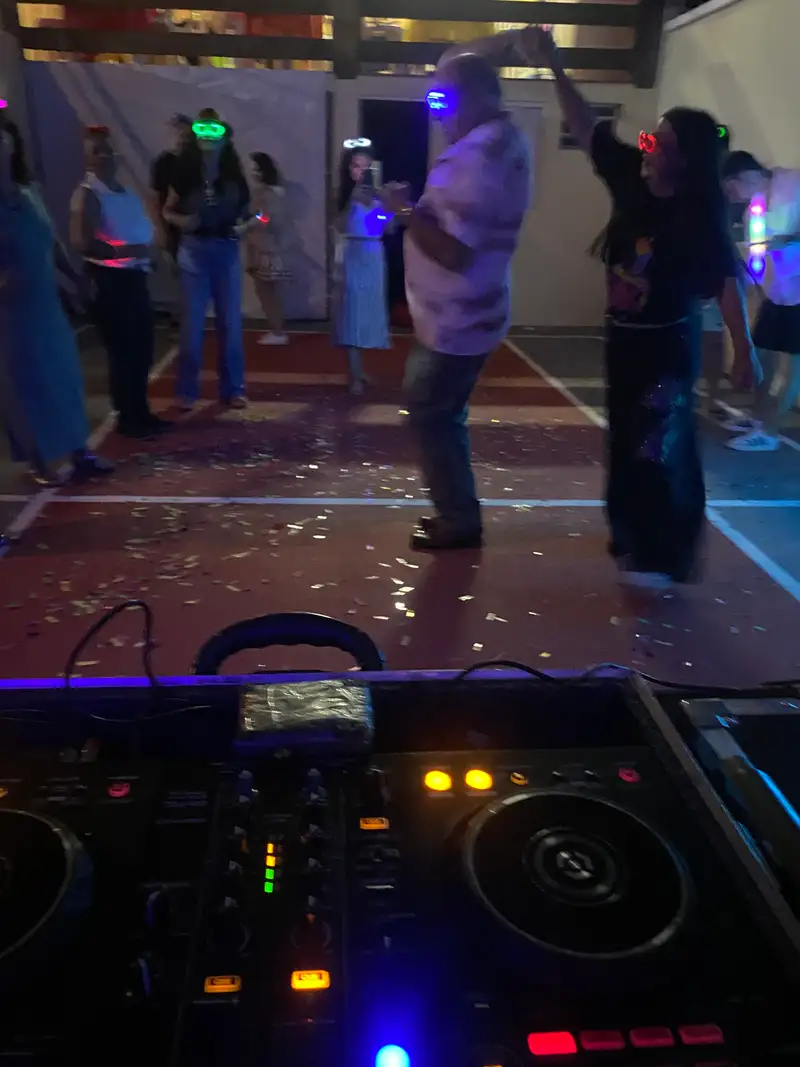 Convidados dançando com óculos de LED na pista, vistos da cabine do DJ