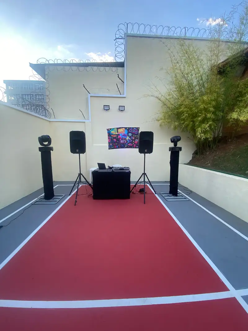 Caixas de som em tripé, moving heads e cabine de DJ montados em uma quadra de condomínio