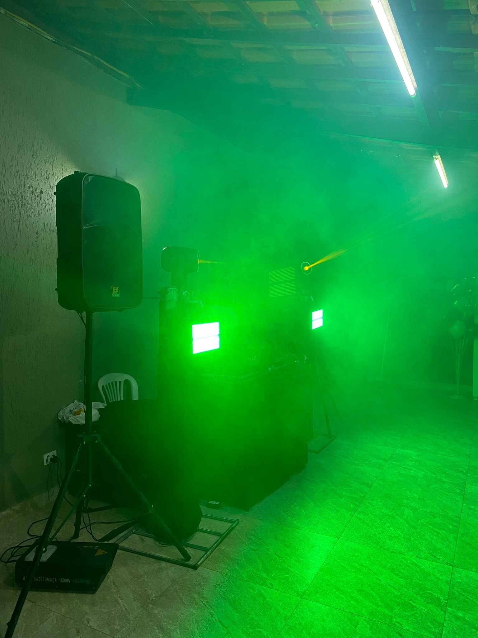 Caixa de som, moving heads e strobos montados ao lado da cabine de DJ, com luz verde e fumaça no salão